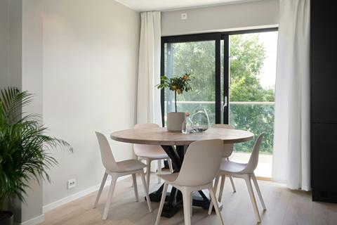 Ronde houten eettafel met vier witte stoelen in een lichte woonkamer met groot raam
