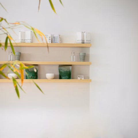 Drie lichte houten wandplanken met verzorgingsproducten aan een witte muur