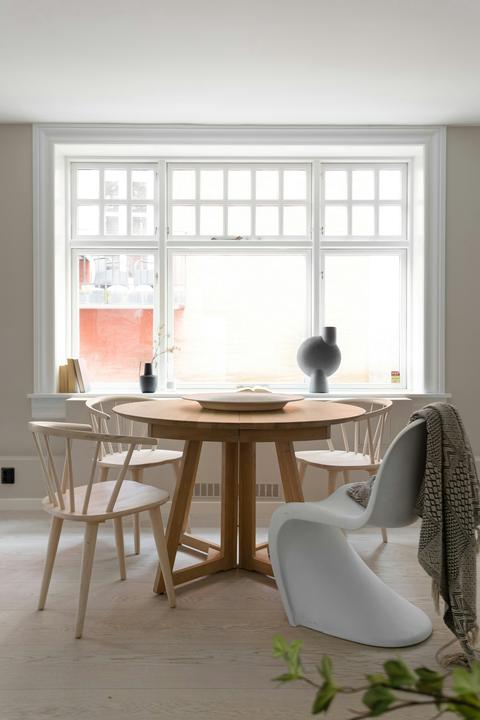 Ronde houten eettafel met massief houten tafelpoten en diverse stoelen voor een groot raam