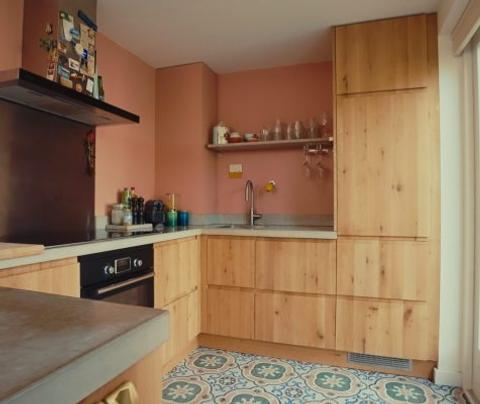 Keuken met houten keukendeurtjes, hoge kasten, roze wanden en een decoratieve tegelvloer
