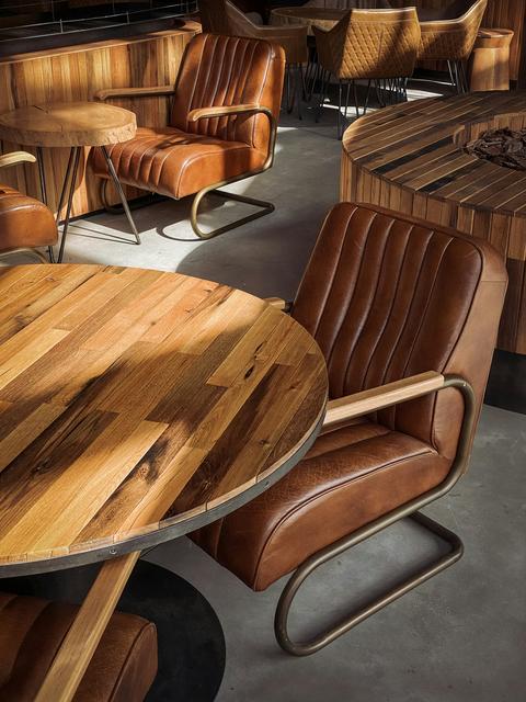 Ronde houten tafels met zwarte tafelpoten en bruine leren stoelen in een sfeervol interieur