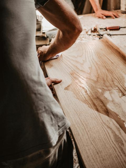 Vakman schuurt een massief kersenhouten tafelblad met doorgaande lamel