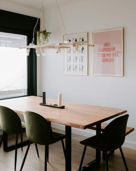 Massief houten eettafel met zwart onderstel en groene stoelen in een licht Scandinavisch interieur