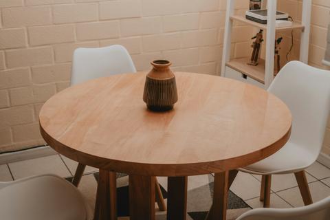 Ronde massief houten tafel met houten tafelpoten, witte stoelen en decoratieve vaas