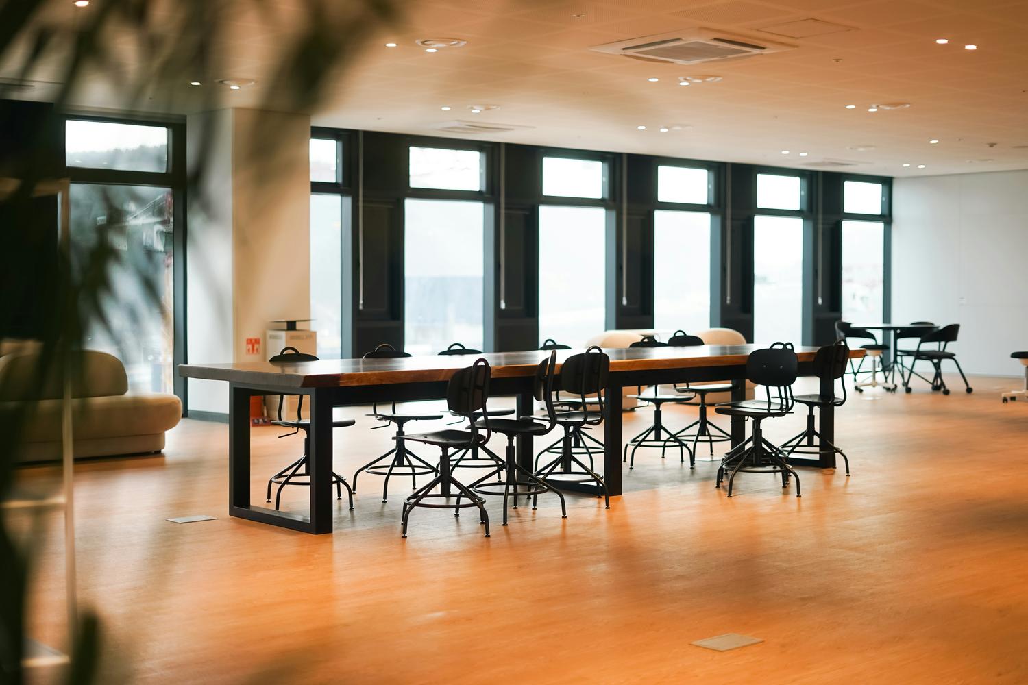 {"nl-NL":"Lang massief houten tafelblad met zwart onderstel en stoelen in een modern kantoorinterieur"}
