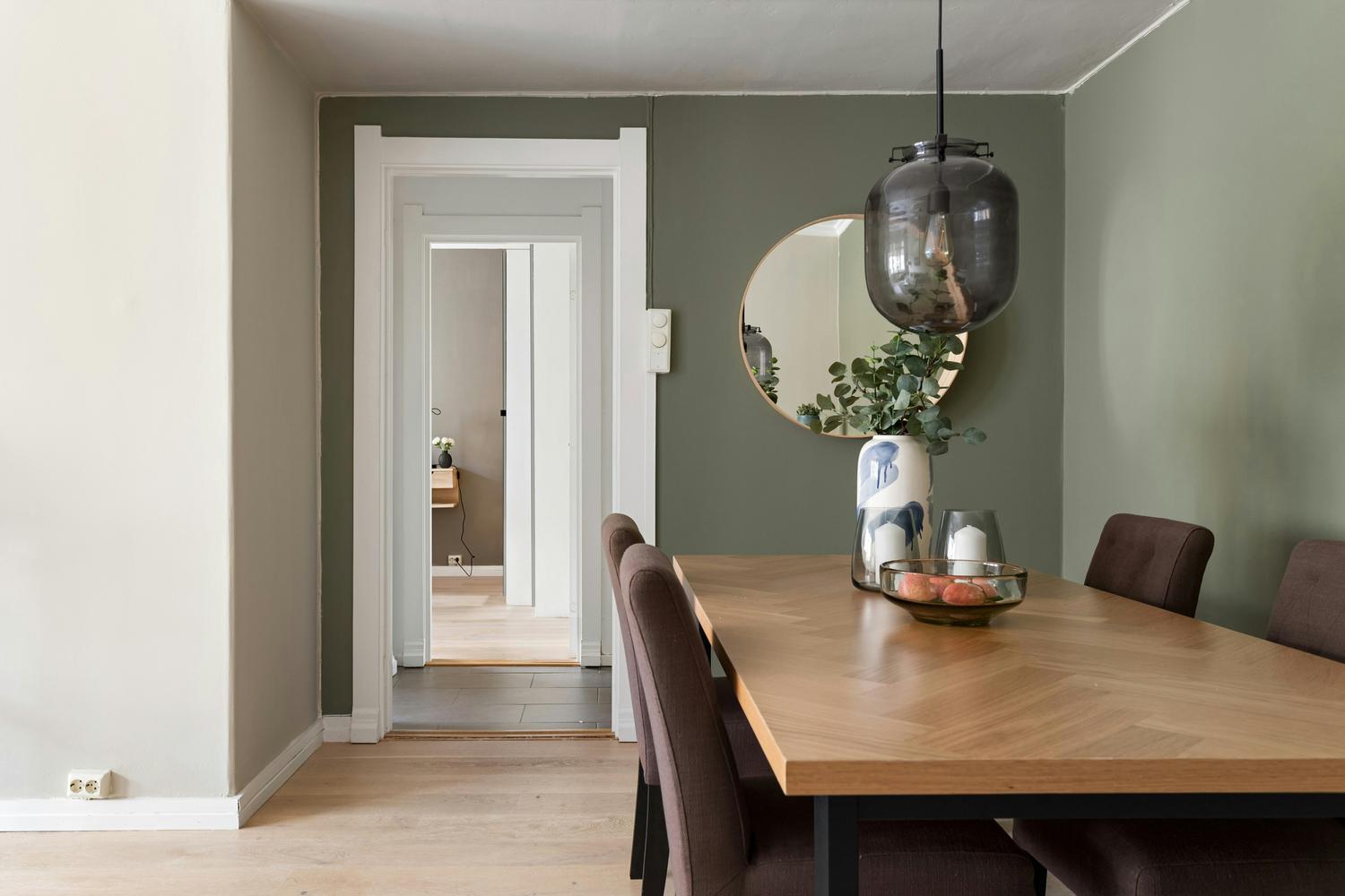 {"nl-NL":"Eetkamer met massief houten tafel, bruine stoelen, groene wand en ronde spiegel"}