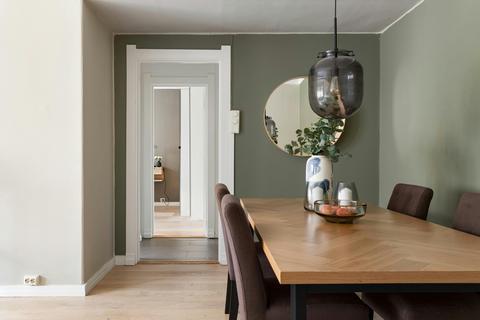 Eetkamer met massief houten tafel, bruine stoelen, groene wand en ronde spiegel